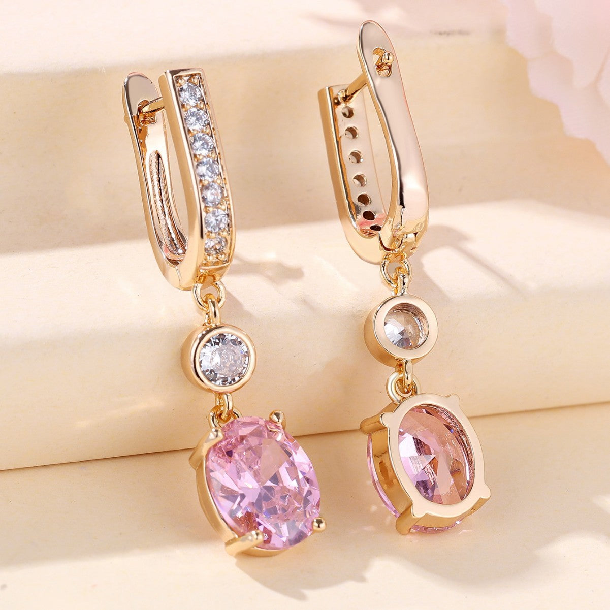 Gold earrings with pink gemstones on a soft beige background