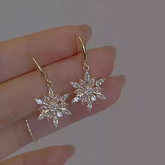 Gold snowflake earrings held on a hand against a plain background