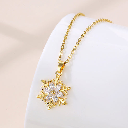 Gold necklace with a snowflake pendant on a white stand against a beige background